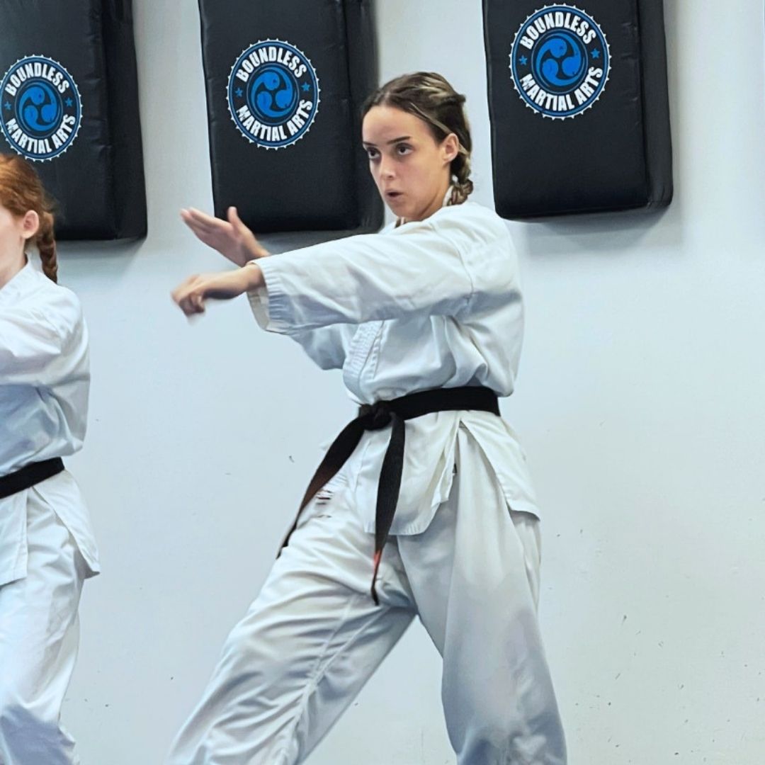 Group of children in martial arts attire posing, some with arms around each other, in a gym.