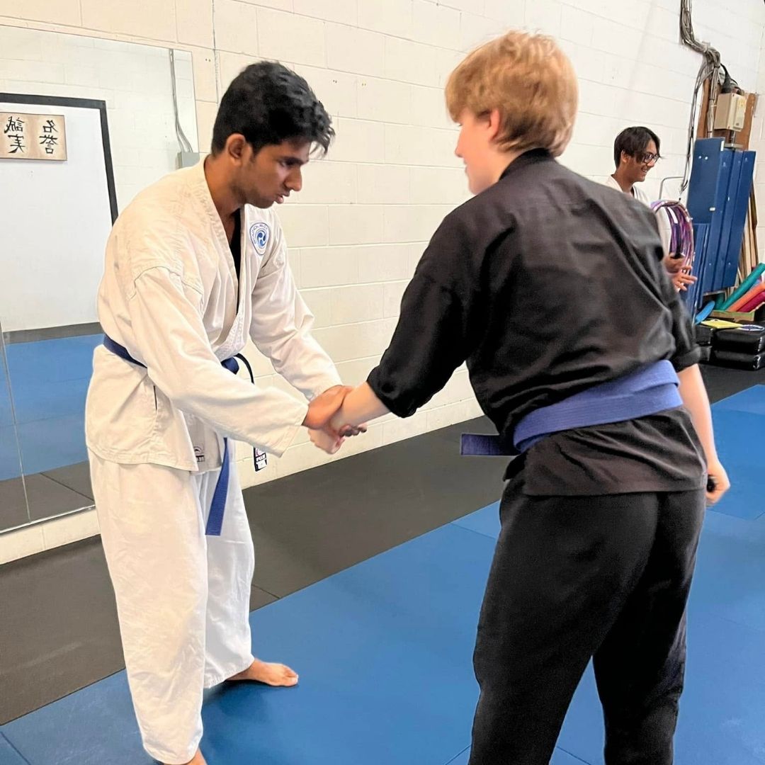 Five people in jiu-jitsu gear pose together in a gym.  Smiling,  some have arms around each other. Machado logo visible.