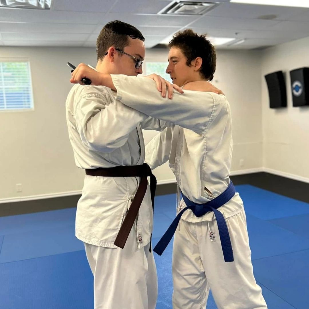 Two people practicing Brazilian Jiu-Jitsu on a mat; one in a black gi, one in a white gi, grappling.