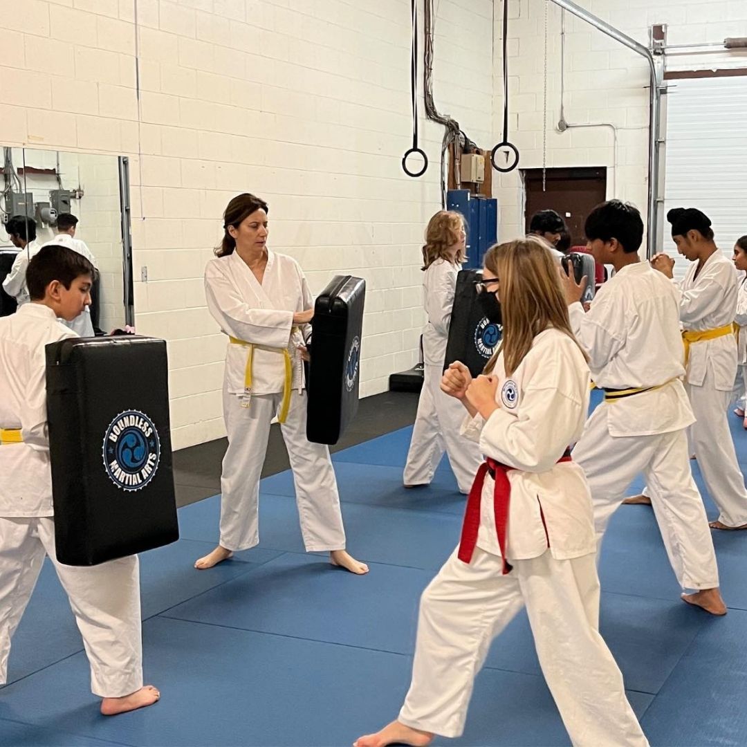 People practicing jiu-jitsu on mats, wearing gis in blue, black, and gray. Active grappling, gym setting.