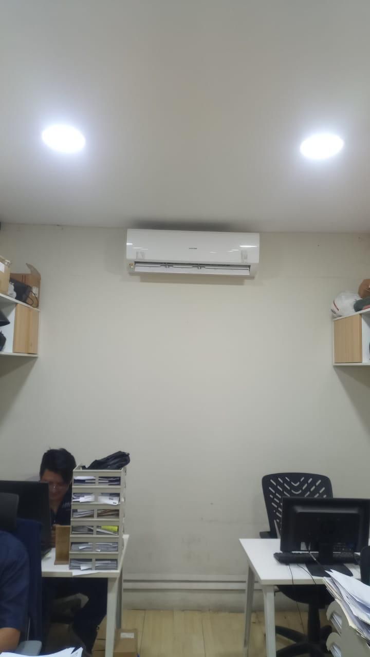 Pequeña oficina con escritorios, ordenadores, estanterías en la pared y aire acondicionado en el techo