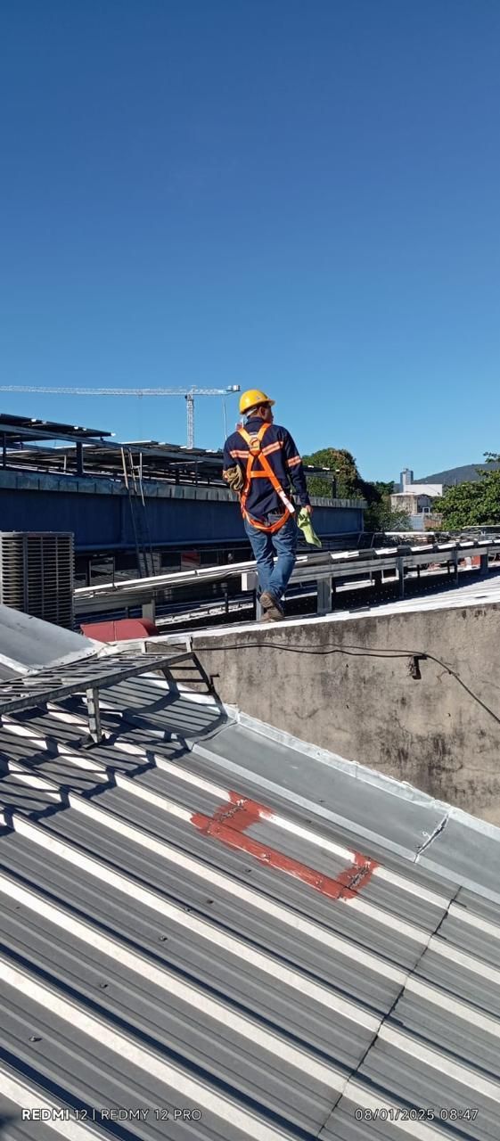 Un trabajador con equipo de seguridad naranja se encuentra en una azotea junto a paneles