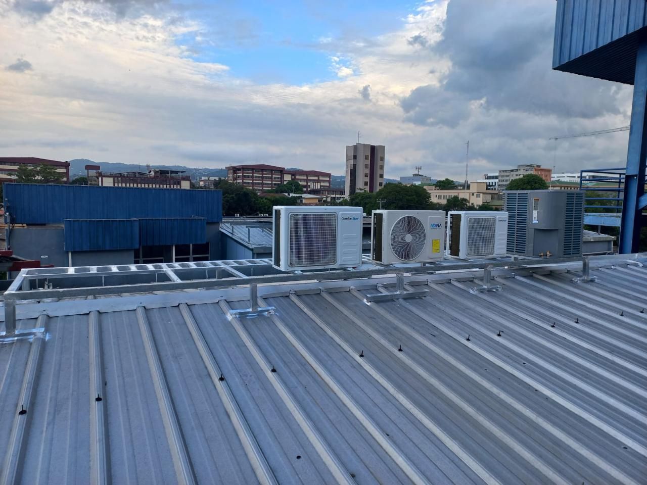 Azotea con techo de metal plateado, unidades de climatización y el horizonte de la ciudad bajo un cielo nublado.