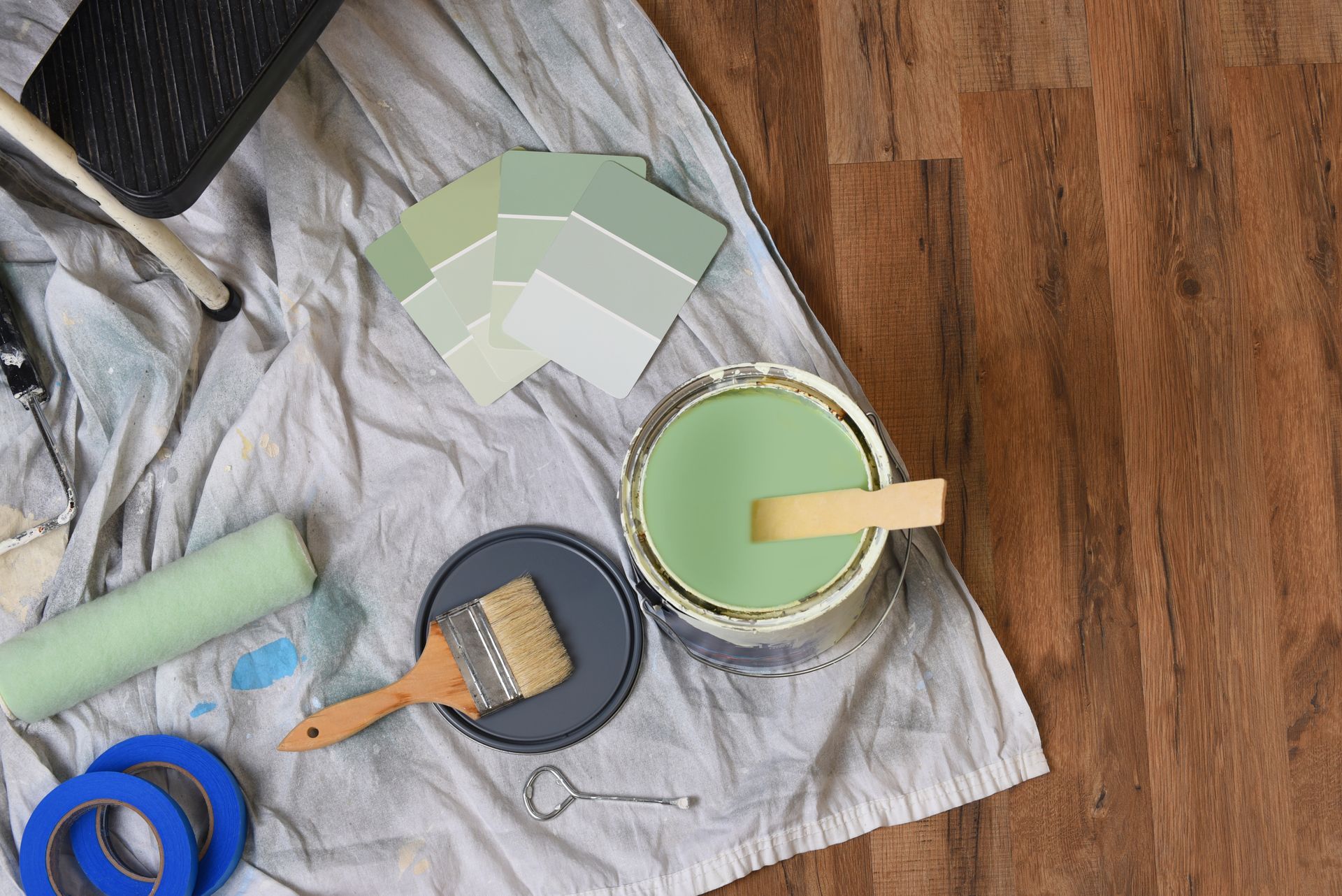 Paint supplies, color swatches, and tools arranged on a drop cloth over hardwood flooring.