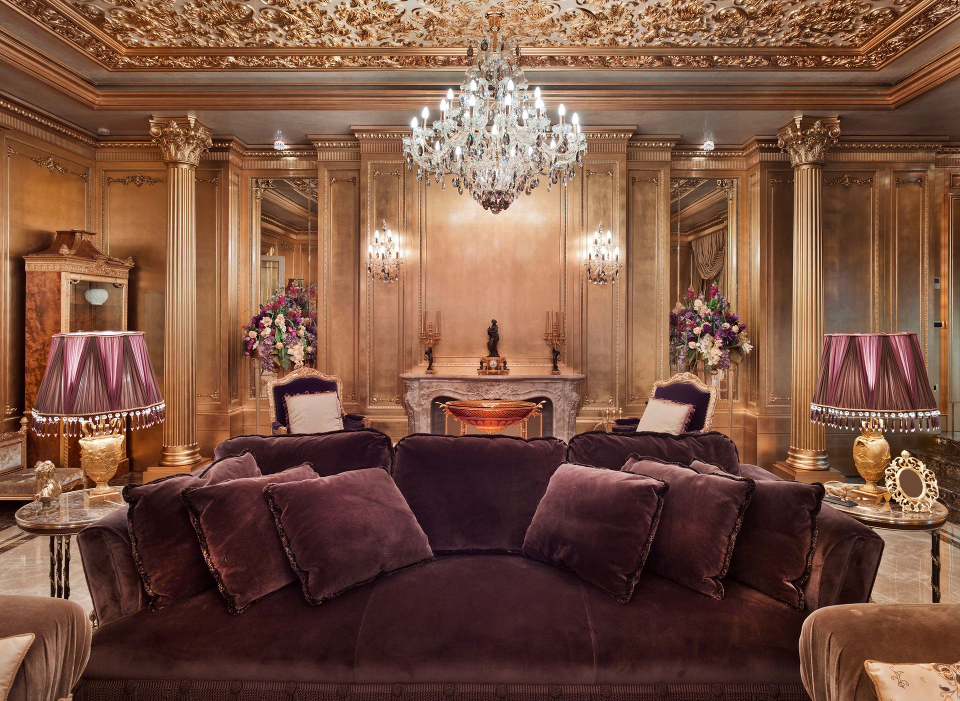 Luxurious gold and purple living room with a large sofa, chandelier, and ornate decor.