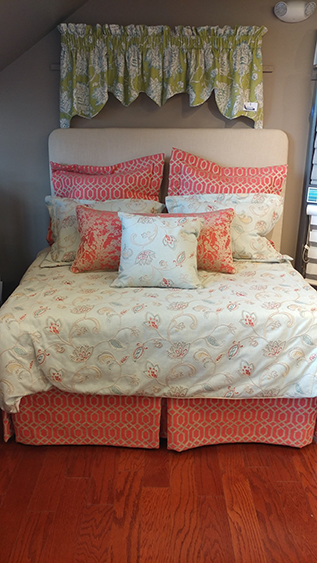 Bed with floral bedding, orange accents, and a matching valance in an attic room.