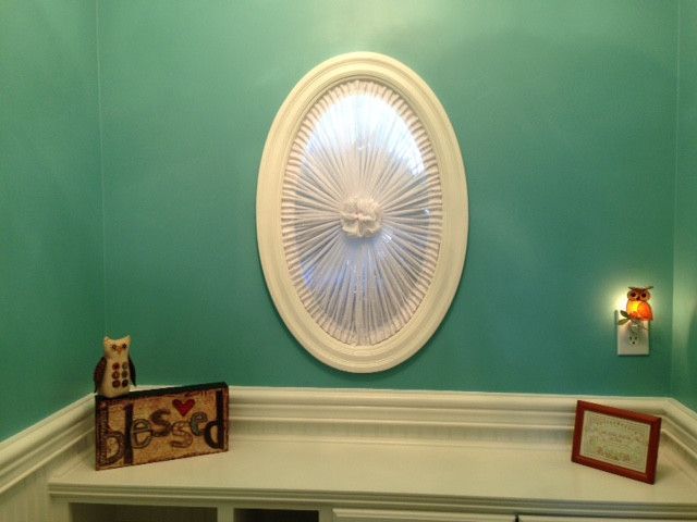 Teal wall with a white oval wall decor, owl nightlight, and decorative items on a white shelf.