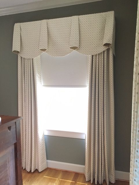 Window with beige curtains, a scalloped valance, and a white window frame. The setting is a room with wooden floors.