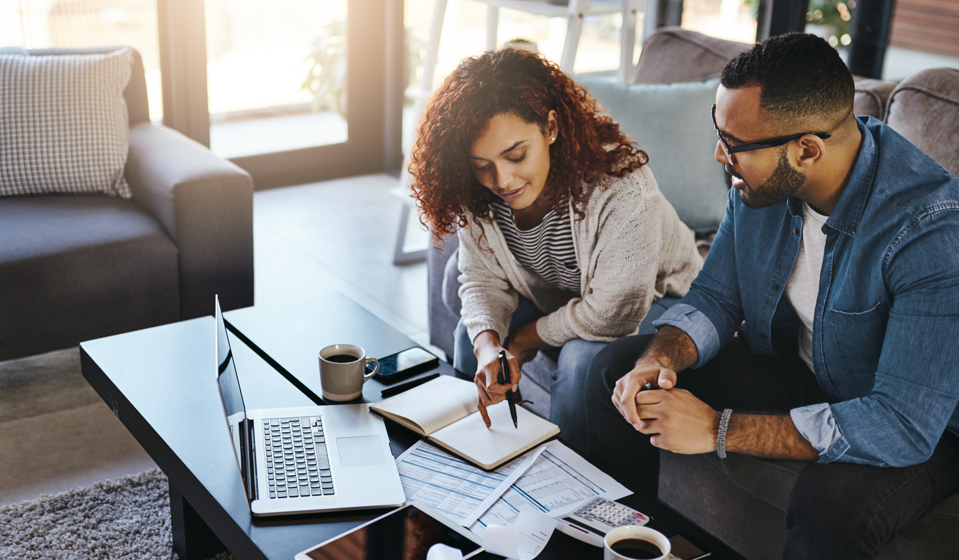 A man and a woman are sitting on a couch looking at a notebook.