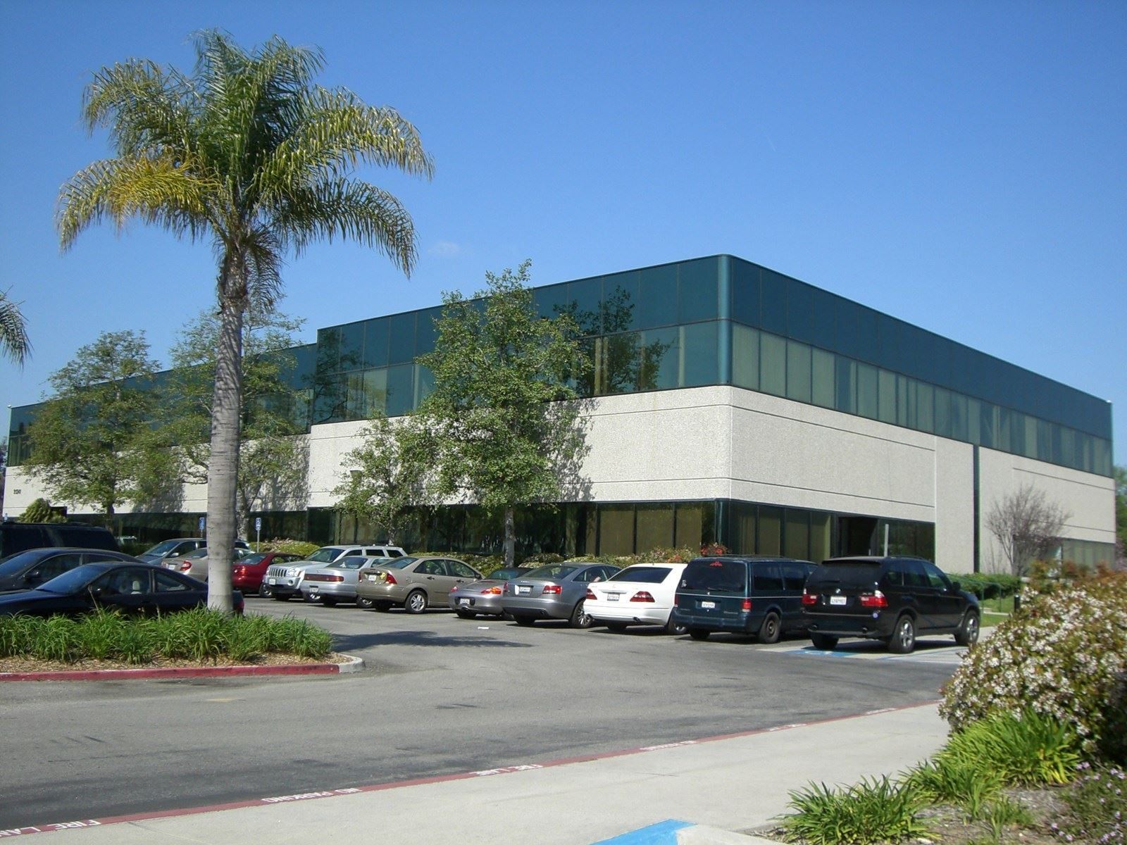 Building exterior with a grassy lawn and trees. Beige and black facade, sunny day.