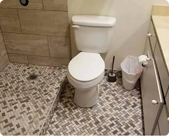 Small bathroom with toilet, mosaic tile floor, wood cabinetry, trash can, and toilet brush holder