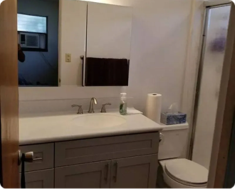 Bathroom with white sink, gray vanity, mirror, toilet, and shower stall.