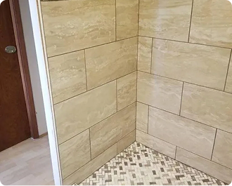 Tiled shower corner with beige stone-look wall tiles and small mosaic floor tiles beside a doorway