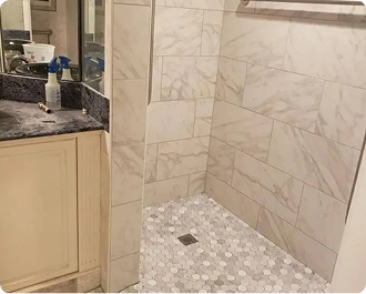 Bathroom shower stall with beige tile and a white pebble shower floor beside a vanity sink.