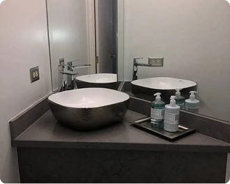 Bathroom sink and mirror with a white basin, gray counter, and soap dispensers on a tray.