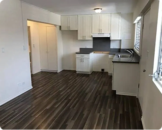 Empty modern kitchen with white cabinets, dark countertops, and dark wood flooring