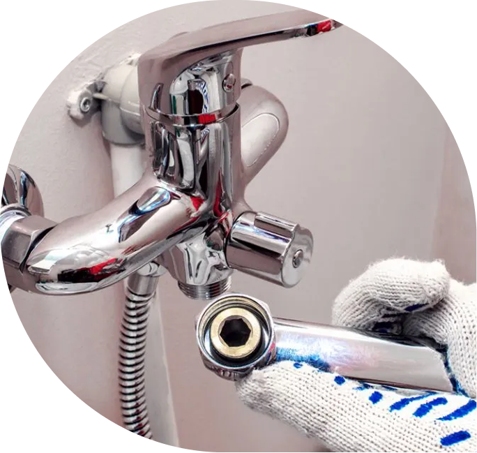 Close-up of a plumber tightening a chrome shower faucet with a wrench, wearing white gloves.