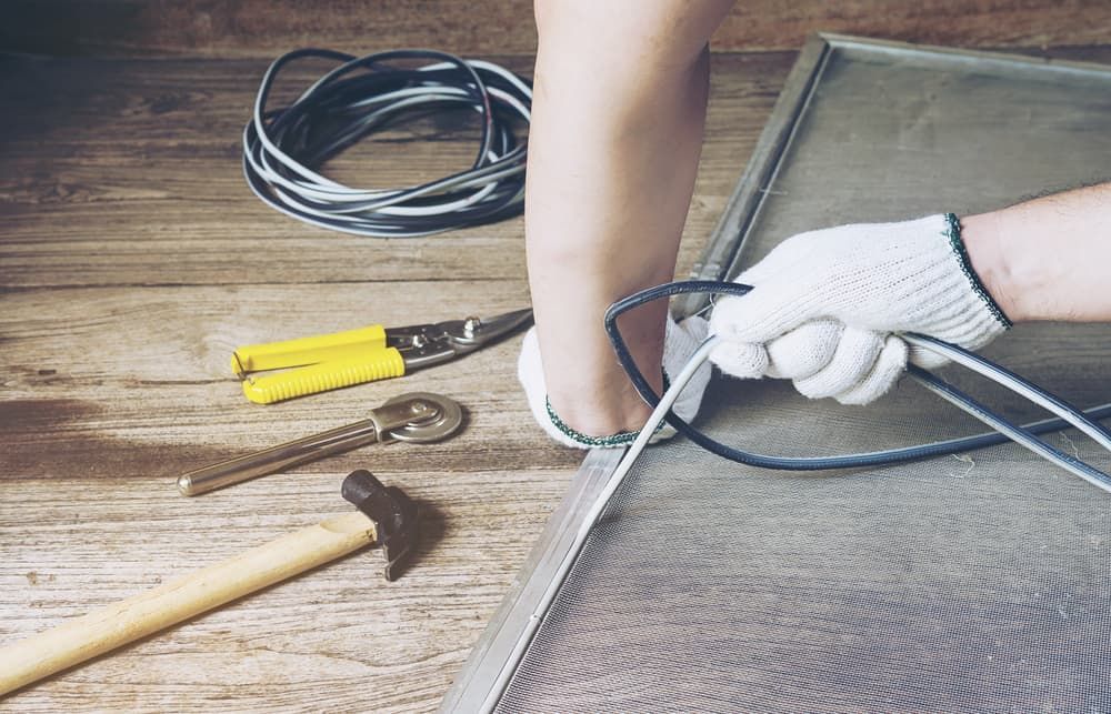 A Person Is Working On A Screen Door On A Wooden Table — Summerland Screens & Awnings In Ballina, NSW