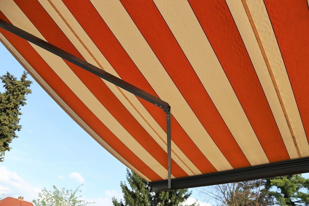 A Red And White Striped Awning With Trees — Summerland Screens & Awnings In Ballina, NSW