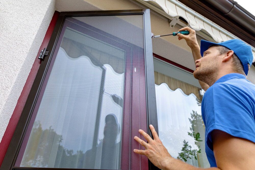 A Man Is Fixing A Screen Door With A Screwdriver — Summerland Screens & Awnings In Lennox Head, NSW