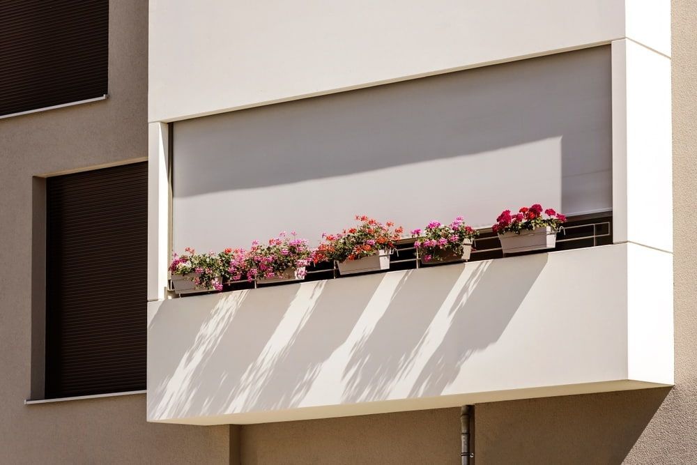 A Balcony With Flowers In Pots On A Building — Summerland Screens & Awnings In Lennox Head, NSW