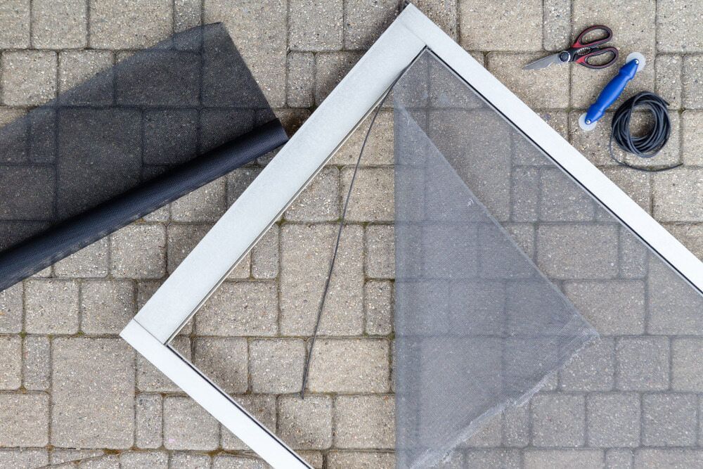 A Mosquito Screen Is Sitting On A Brick Floor Next To A Pair Of Scissors — Summerland Screens & Awnings In Alstonville, NSW