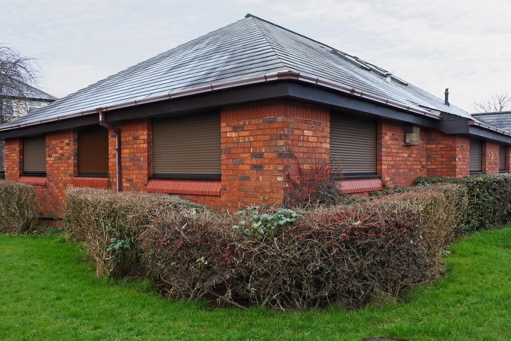 A Brick Building With A Slate Roof And A Hedge In Front Of It — Summerland Screens & Awnings In Alstonville, NSW