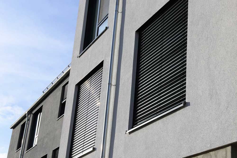 A Grey Building With Black Blinds On The Windows — Summerland Screens & Awnings In Ballina, NSW