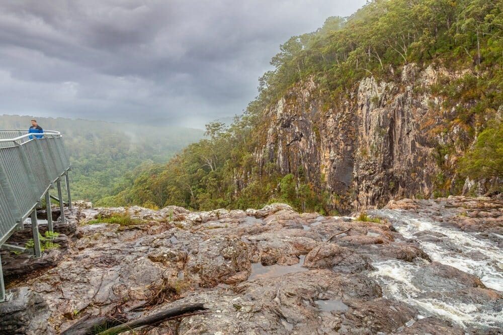 A Man Is Standing On A Bridge Overlooking A River — Summerland Screens & Awnings In Alstonville, NSW