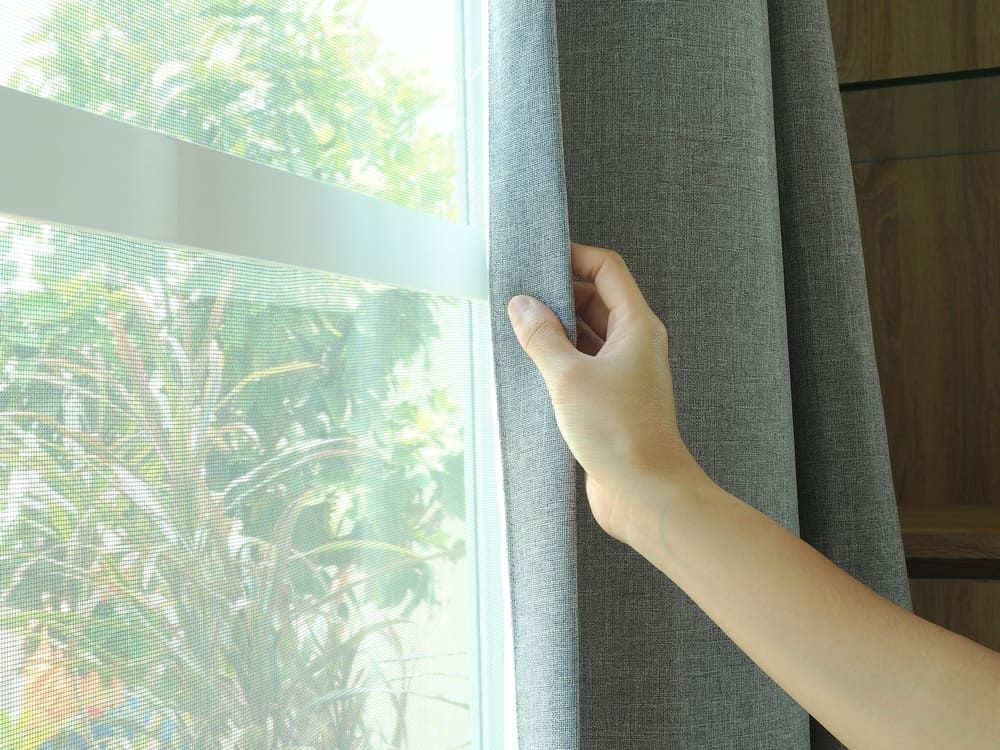 A Person Is Opening A Window With A Gray Curtain — Summerland Screens & Awnings In Evans Head, NSW
