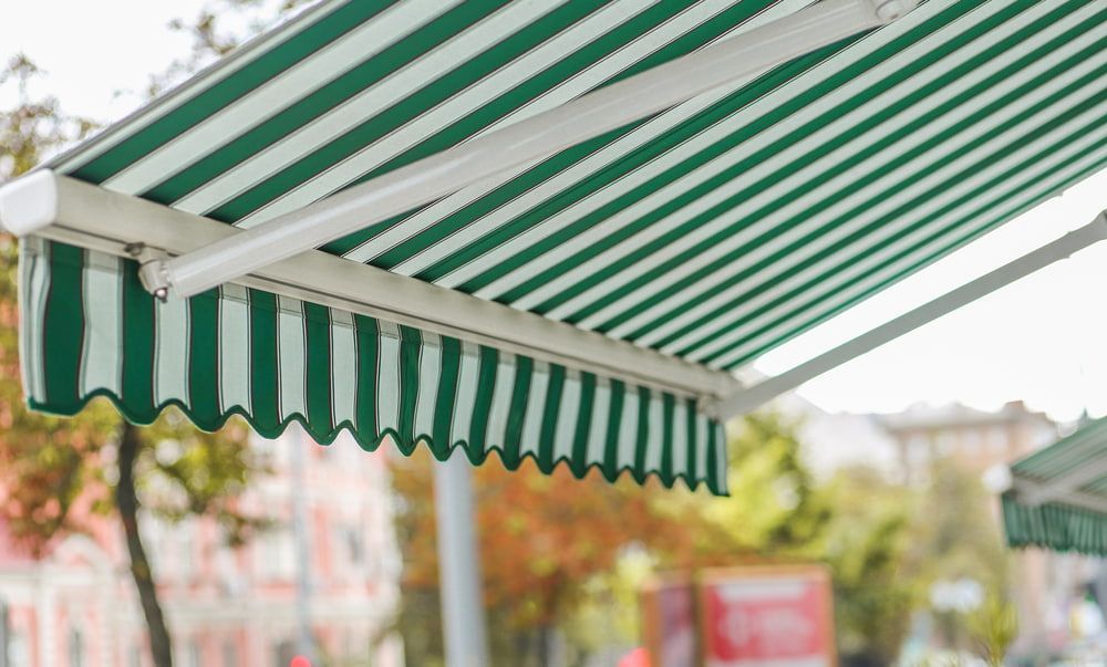 A Green And White Striped Awning Is Hanging From The Side Of A Building — Summerland Screens & Awnings In Lismore, NSW