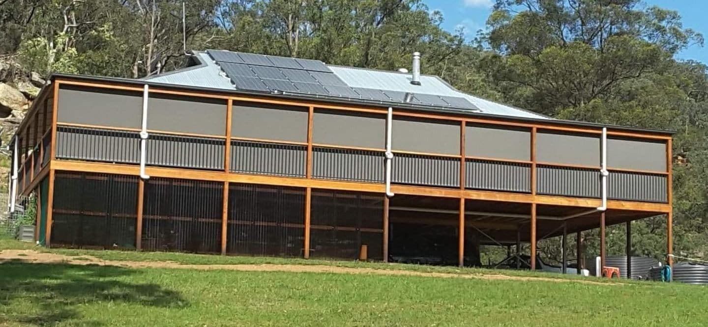 A Large House With A Large Deck Is Sitting On Top Of A Grassy Hill — Summerland Screens & Awnings In Lismore, NSW