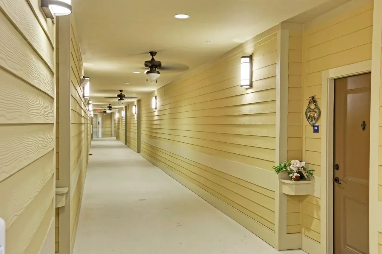 Long beige interior hallway in an apartment building with doors along both walls and ceiling lights.