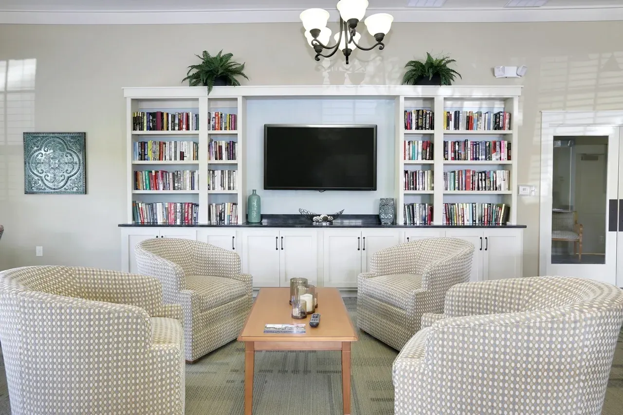 Community lounge with four patterned chairs around a wooden coffee table and a built-in bookshelf with a TV.