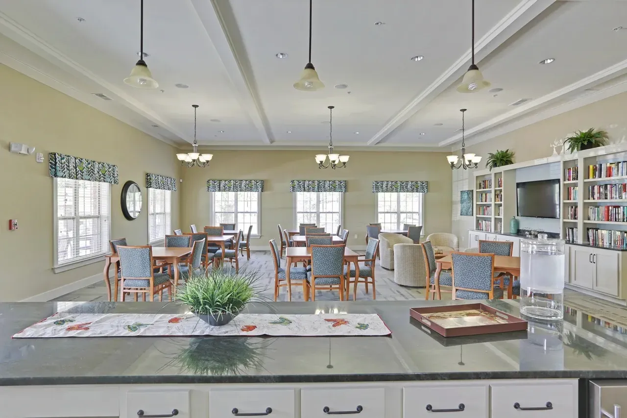 Bright communal lounge with round tables, upholstered chairs, and a kitchen island.
