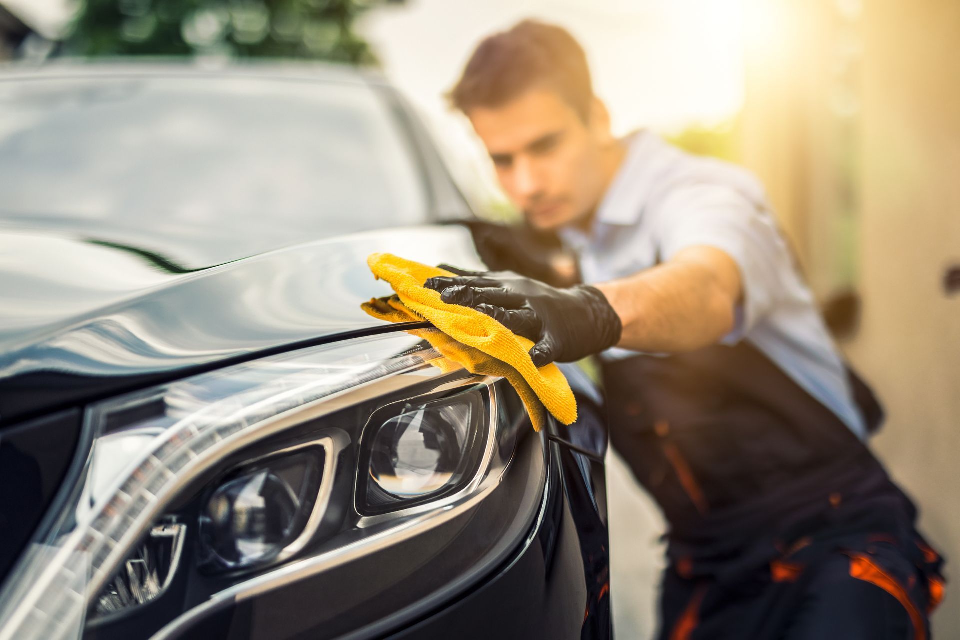A worker wipes the front headlight of a car with a yellow cloth during detailing. A worker wipes the front headlight of a car with a yellow cloth during detailing.