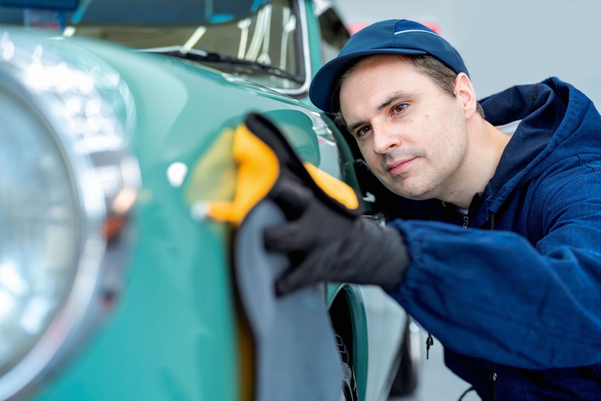 An auto detailing worker cleaning and polishing a car with a rag.