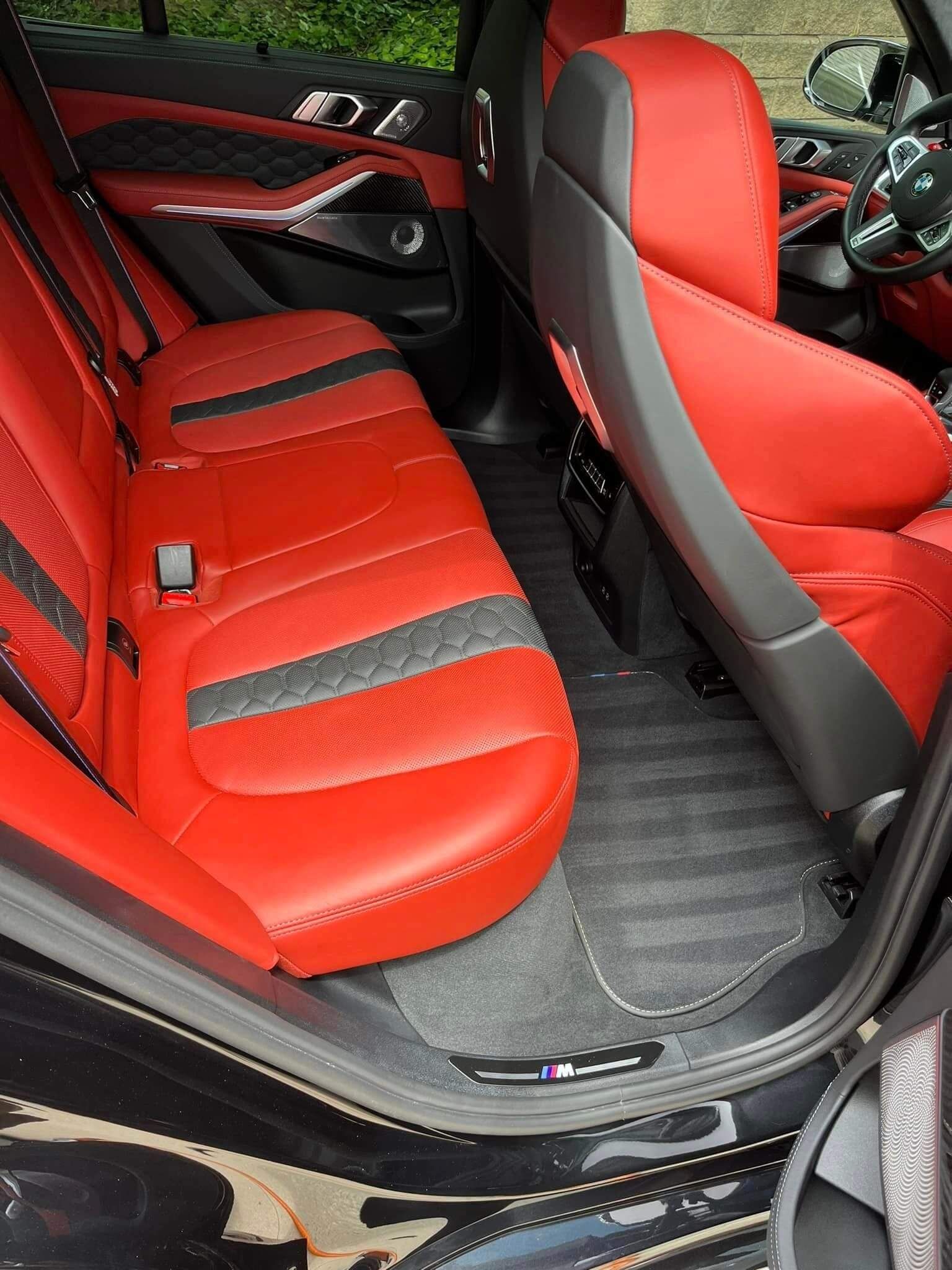 The rear interior of a vehicle featuring vibrant red leather seats with grey accents and black carpeting.