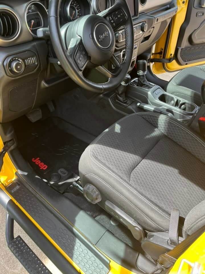 The interior of a yellow Jeep, showing the steering wheel, driver's seat, and a floor mat with the red Jeep logo.