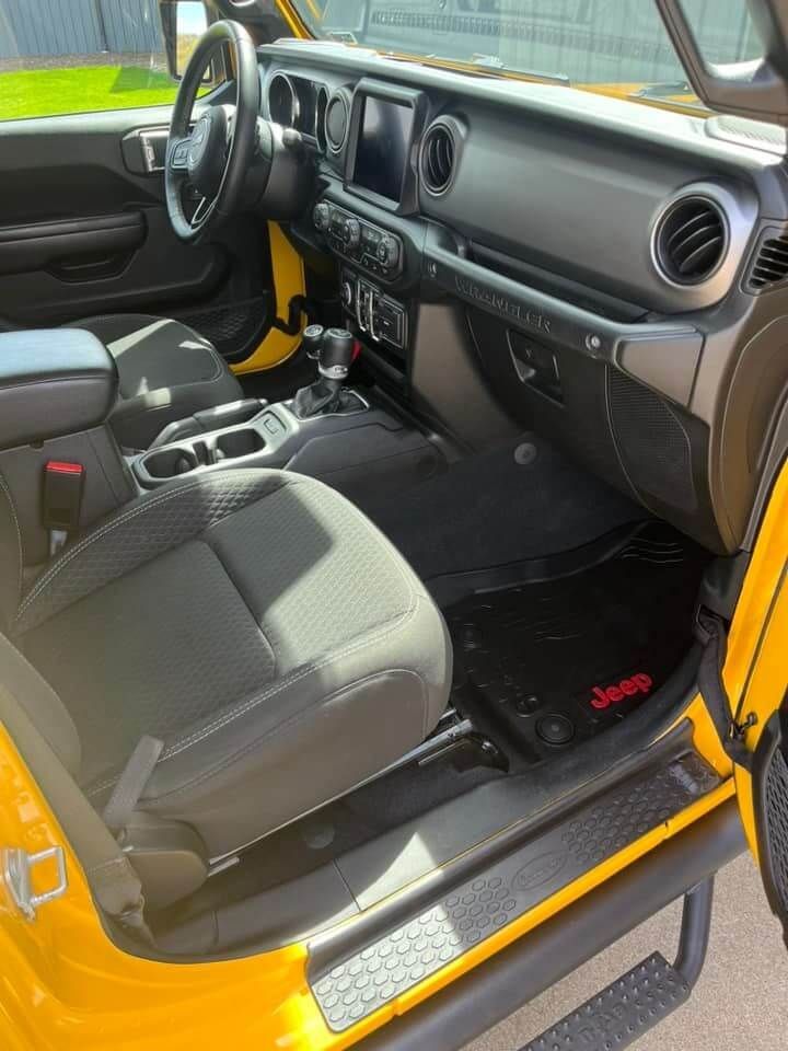 The interior of a yellow Jeep with grey cloth seats, a black dashboard, and floor mats featuring a red Jeep logo.
