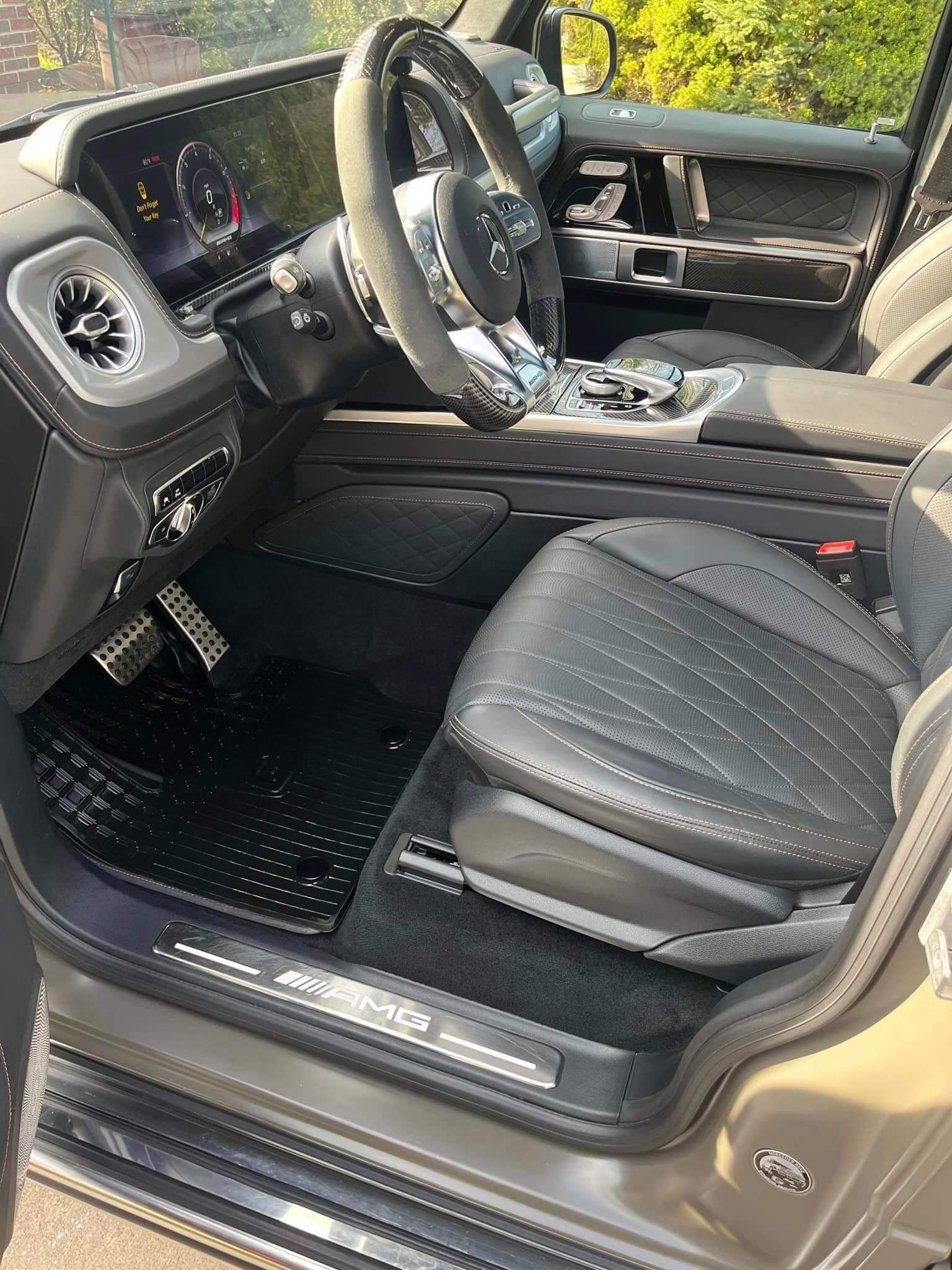 Driver side interior of a luxury Mercedes-Benz G-Class featuring diamond-stitched leather seats and AMG door sills.