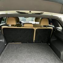 The view looking into the empty trunk of a vehicle, showing the folded rear seats with beige headrests and grey carpeting.