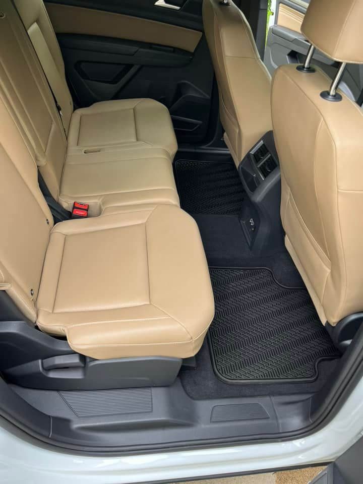 A car's interior view showing tan leather back seats and dark, textured rubber floor mats.
