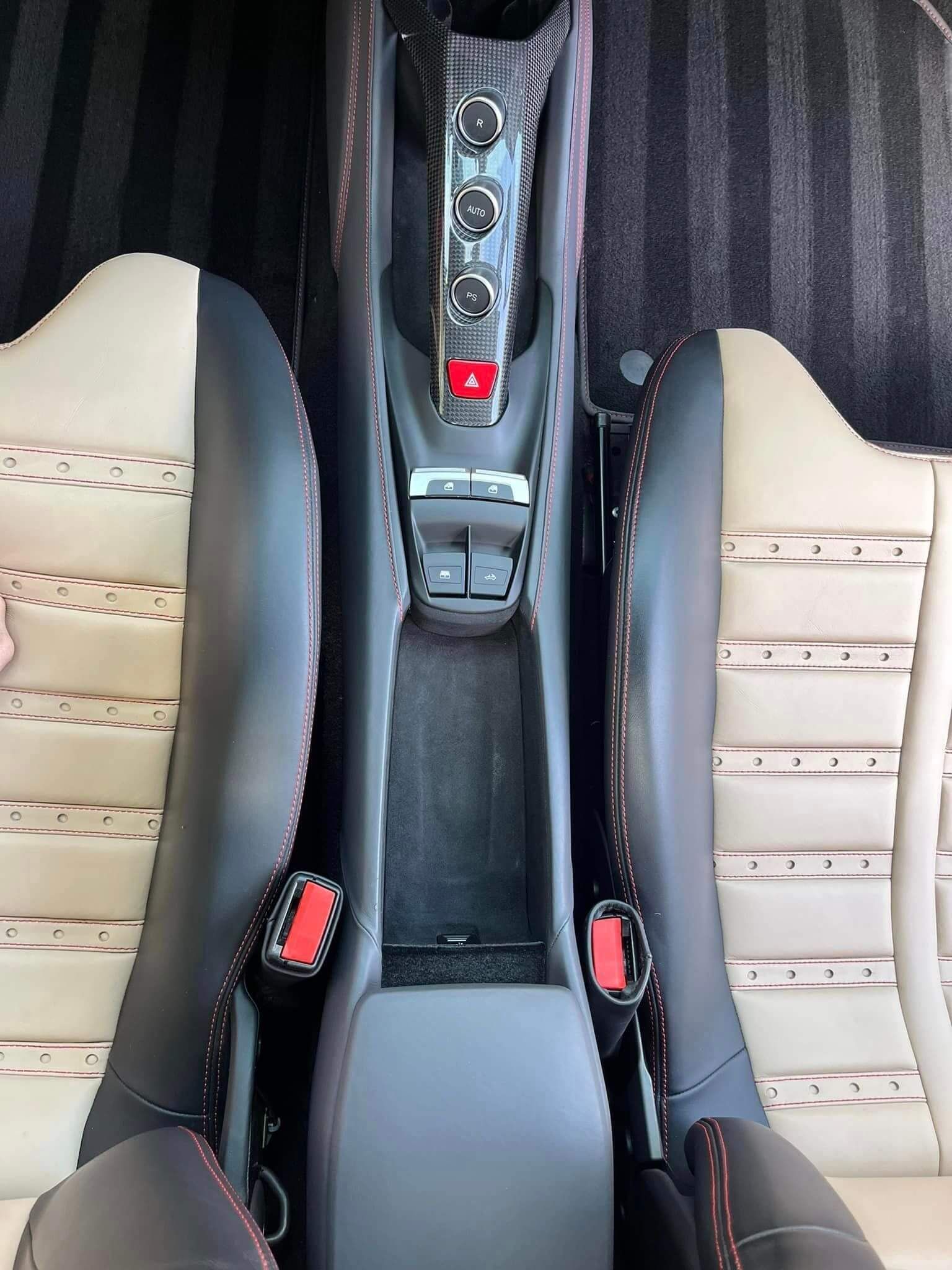 A top-down view of a car interior featuring tan and black leather seats, a center console, and red seatbelt buckles.