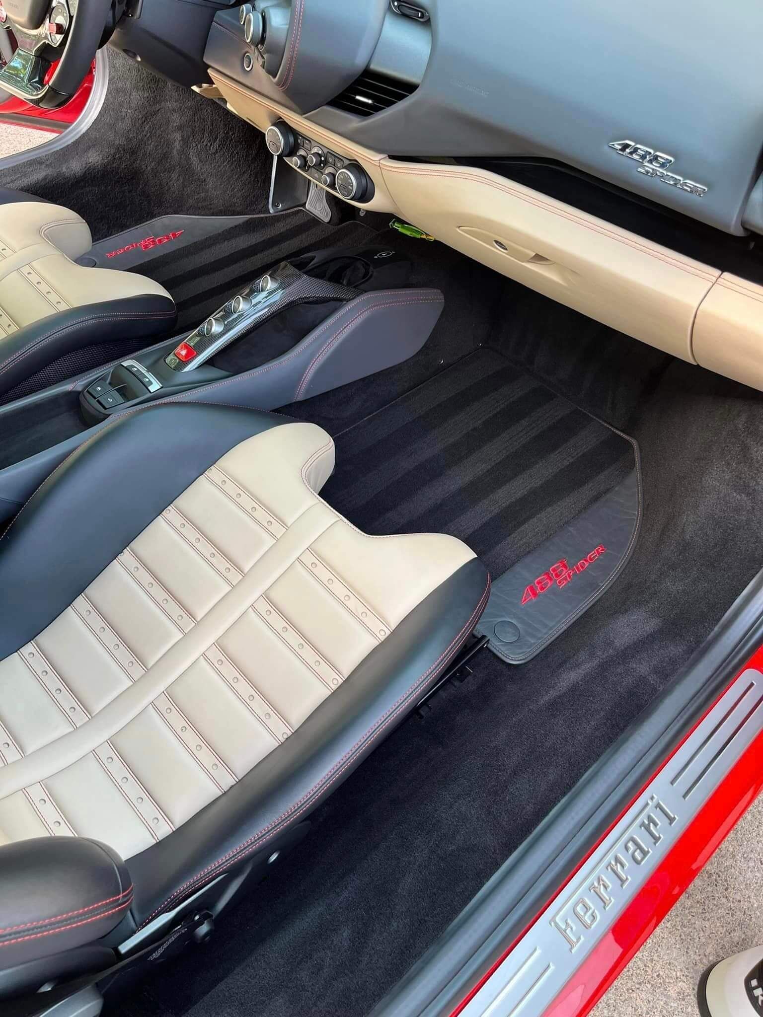 Interior of a Ferrari with beige and black leather seats, a red stitched dashboard, and floor mats with a red emblem.