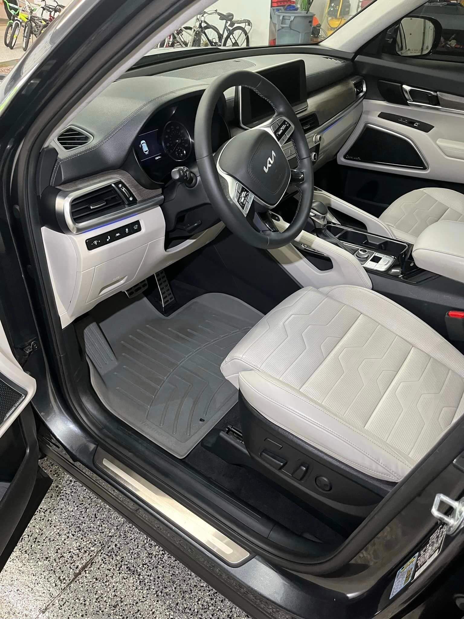 Interior view of a vehicle featuring light gray leather seats, a dark dashboard, and a steering wheel with a Kia emblem.