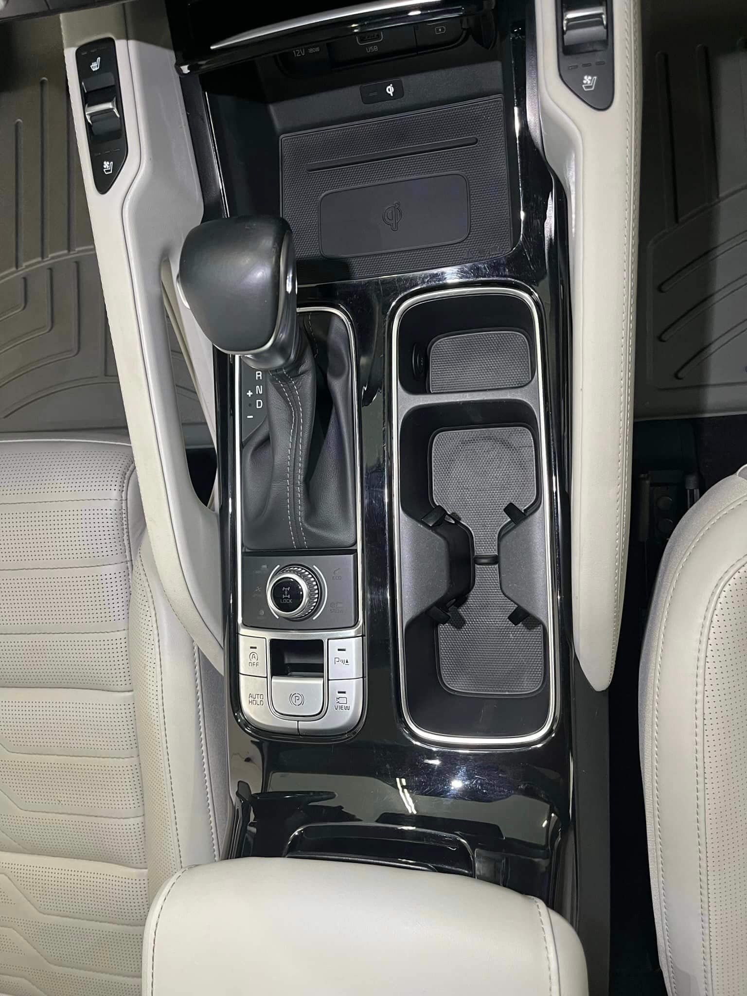 A top-down view of a luxury car's center console featuring a gear shifter, cup holders, and white leather trim.