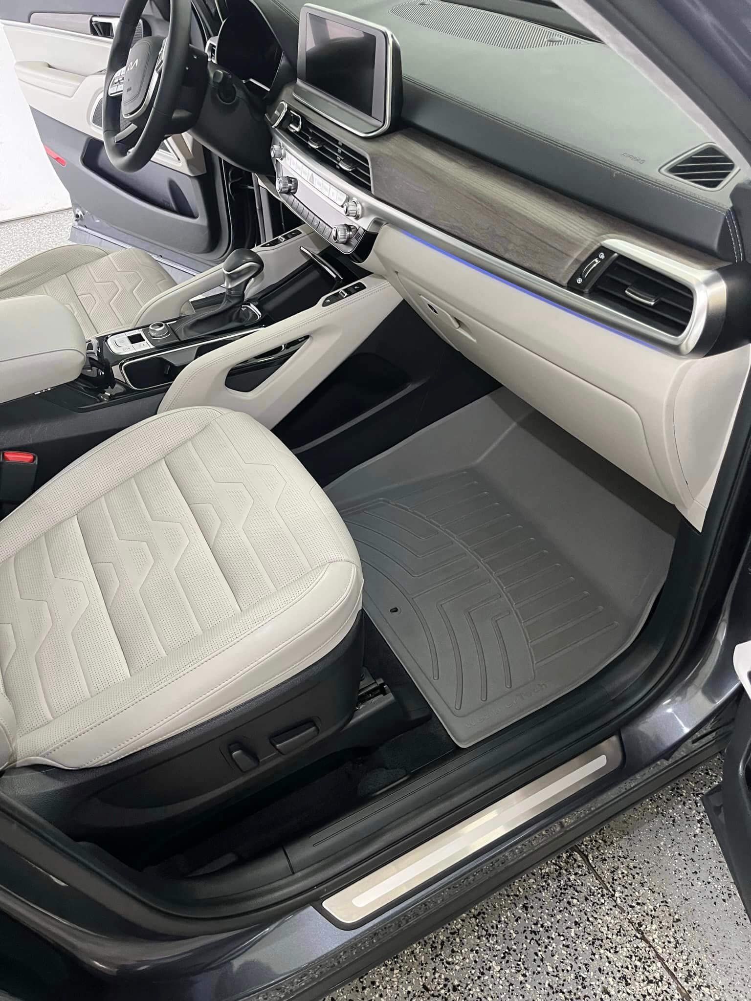 Interior of a car showing a light-colored passenger seat, dashboard, touchscreen, and gray rubber floor mat.