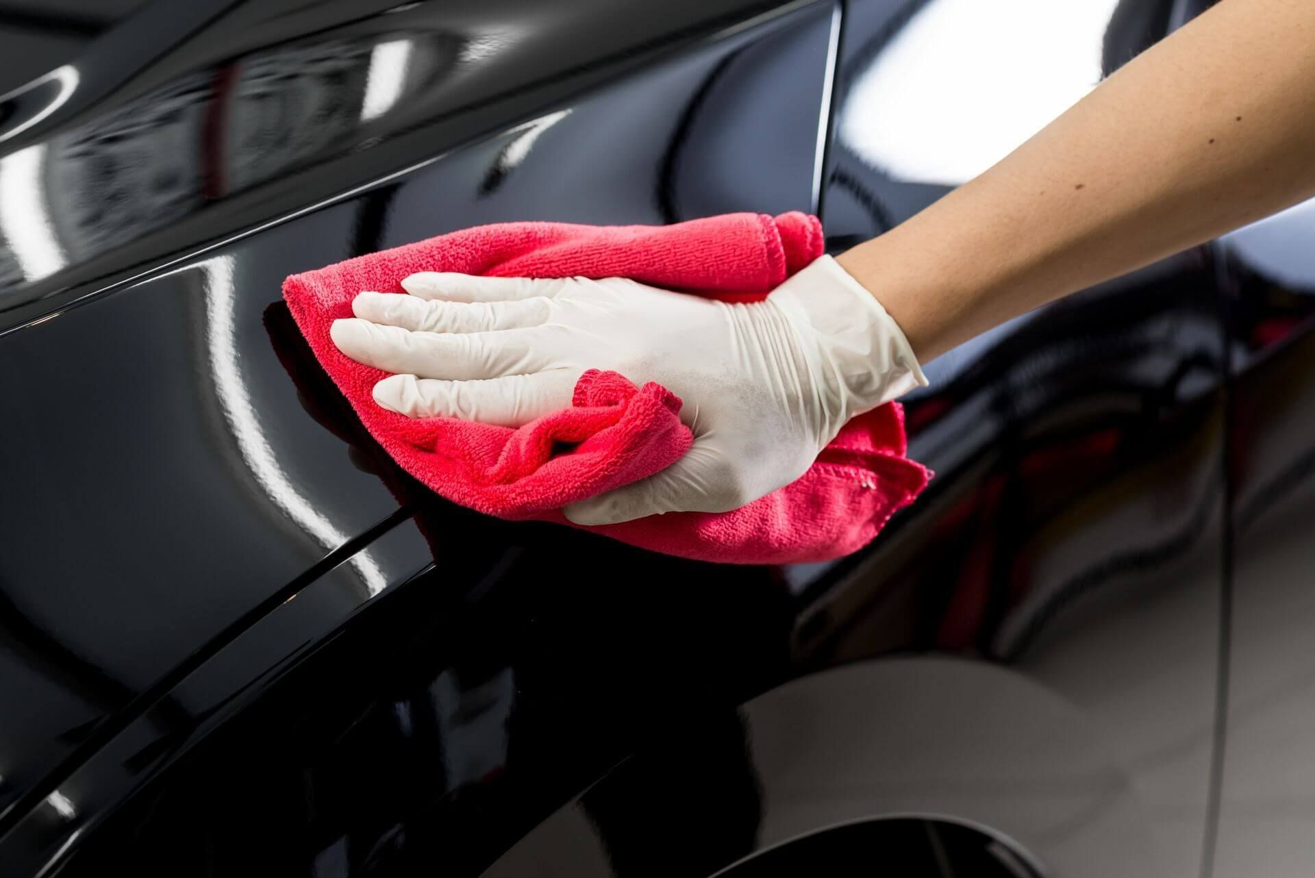 A person is cleaning a car with a towel and gloves.