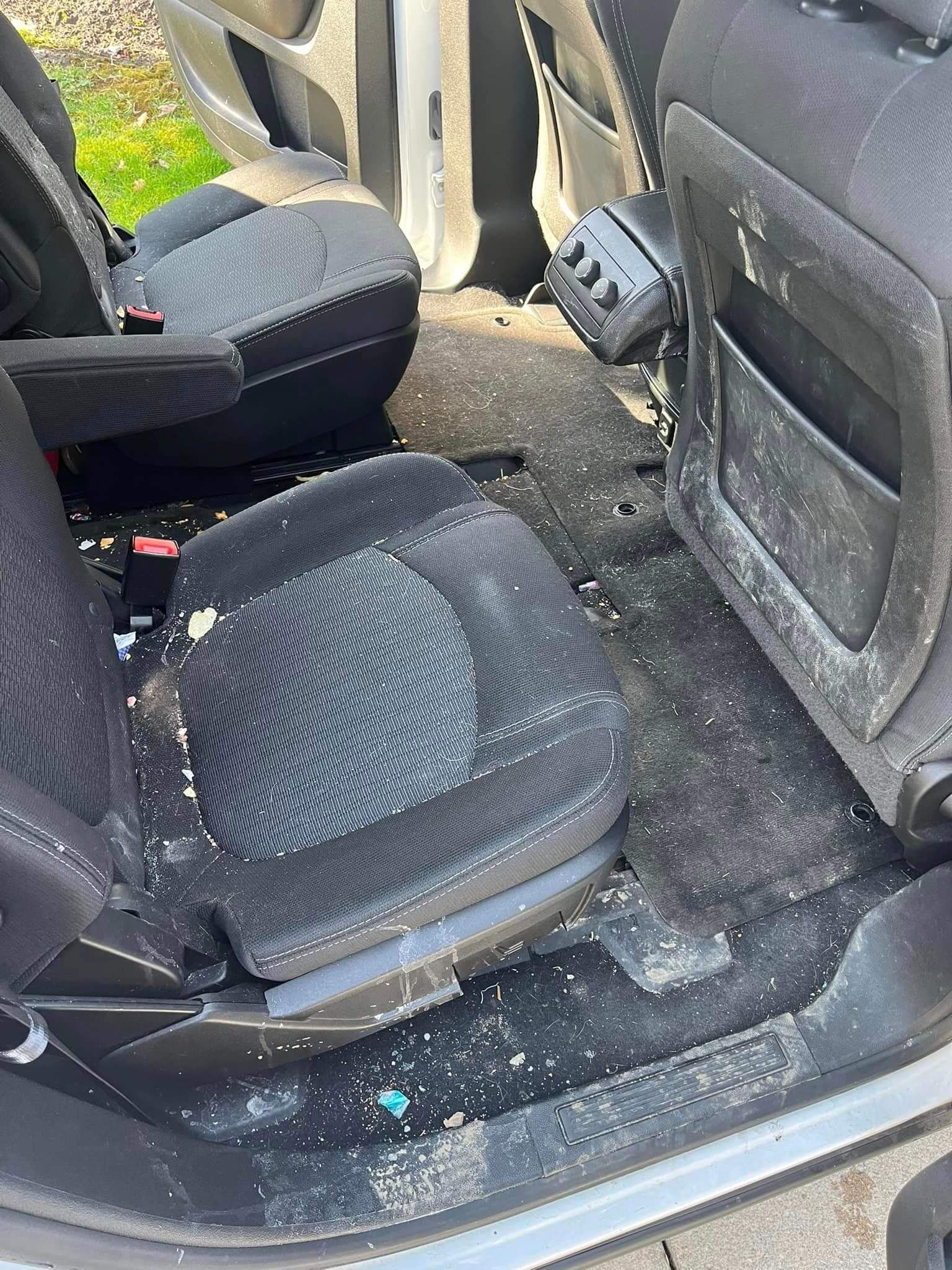 The interior of a car back seat covered in broken glass fragments from a shattered window.